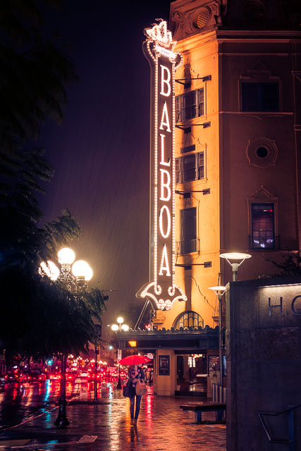 Woman with red umbrella in the rain in front of Balboa Theatre in the Gaslamp Quarter, Downtown San Diego.