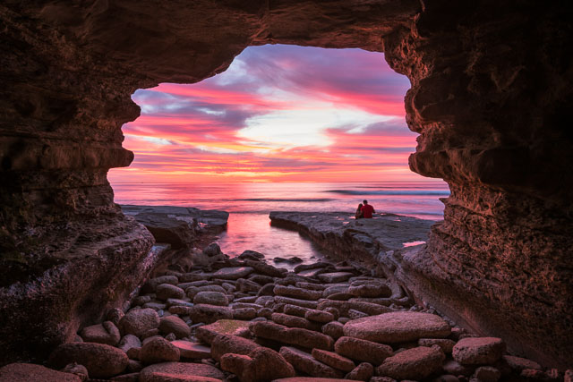 Looking out of a sea cave at Sunset Cliffs. In the distance is a couple enjoying the sunset.