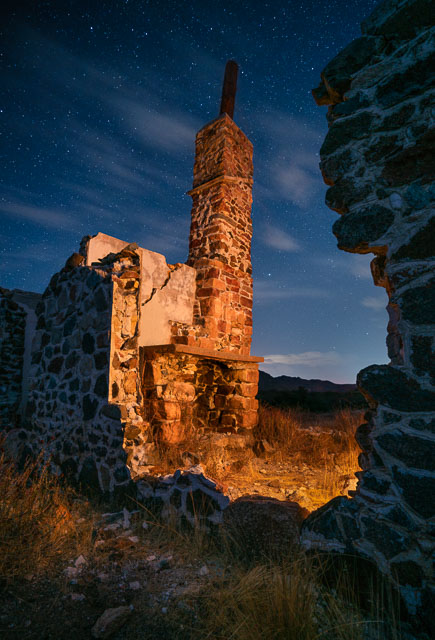 An abandoned home in east San Diego county under the night sky. All that remains is a chimney and a partially standing wall.