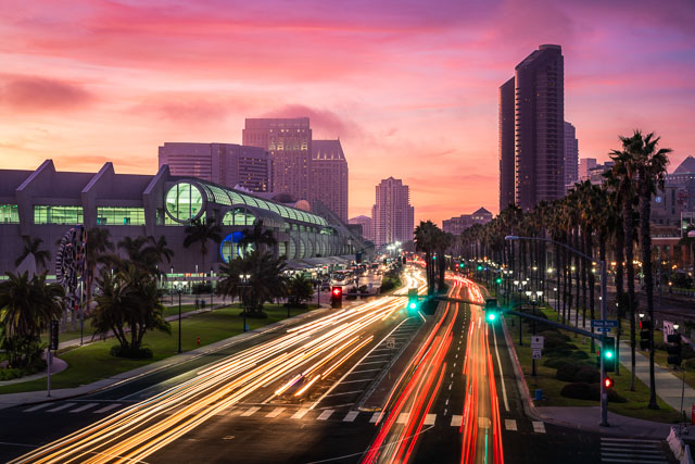 Sunset over downtown and harbor drive with light trails from vehicles. The sky is misty pink as there is fog being lit up at sunset.