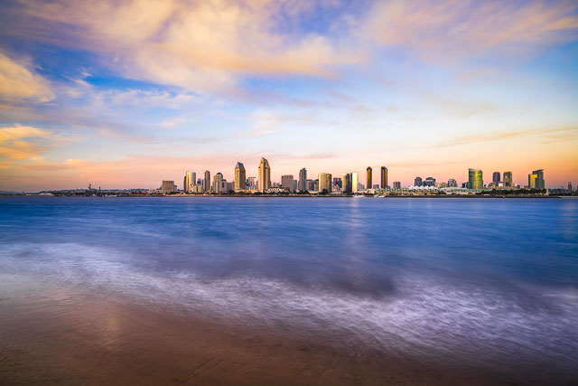 The San Diego skyline with clouds blowing in from offshore that give the image a dream feel. The waves are washing up against the sandy shoreline.
